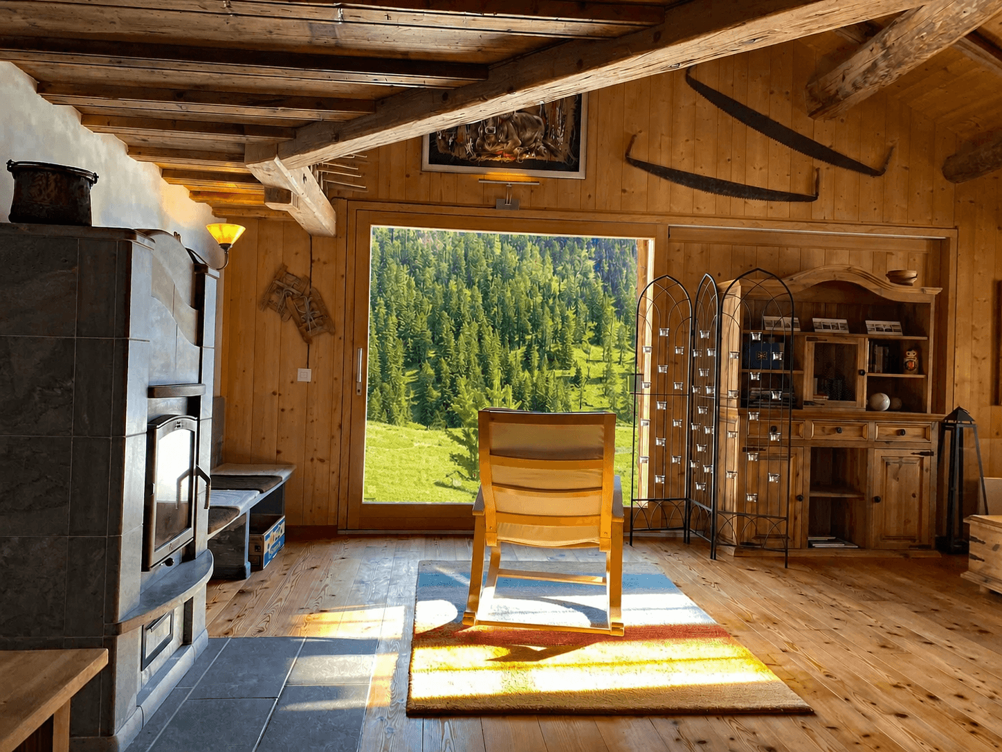 Schaukelstuhl am grossen Fenster der Wohnstube mit Blick auf die grüne Bergwiese