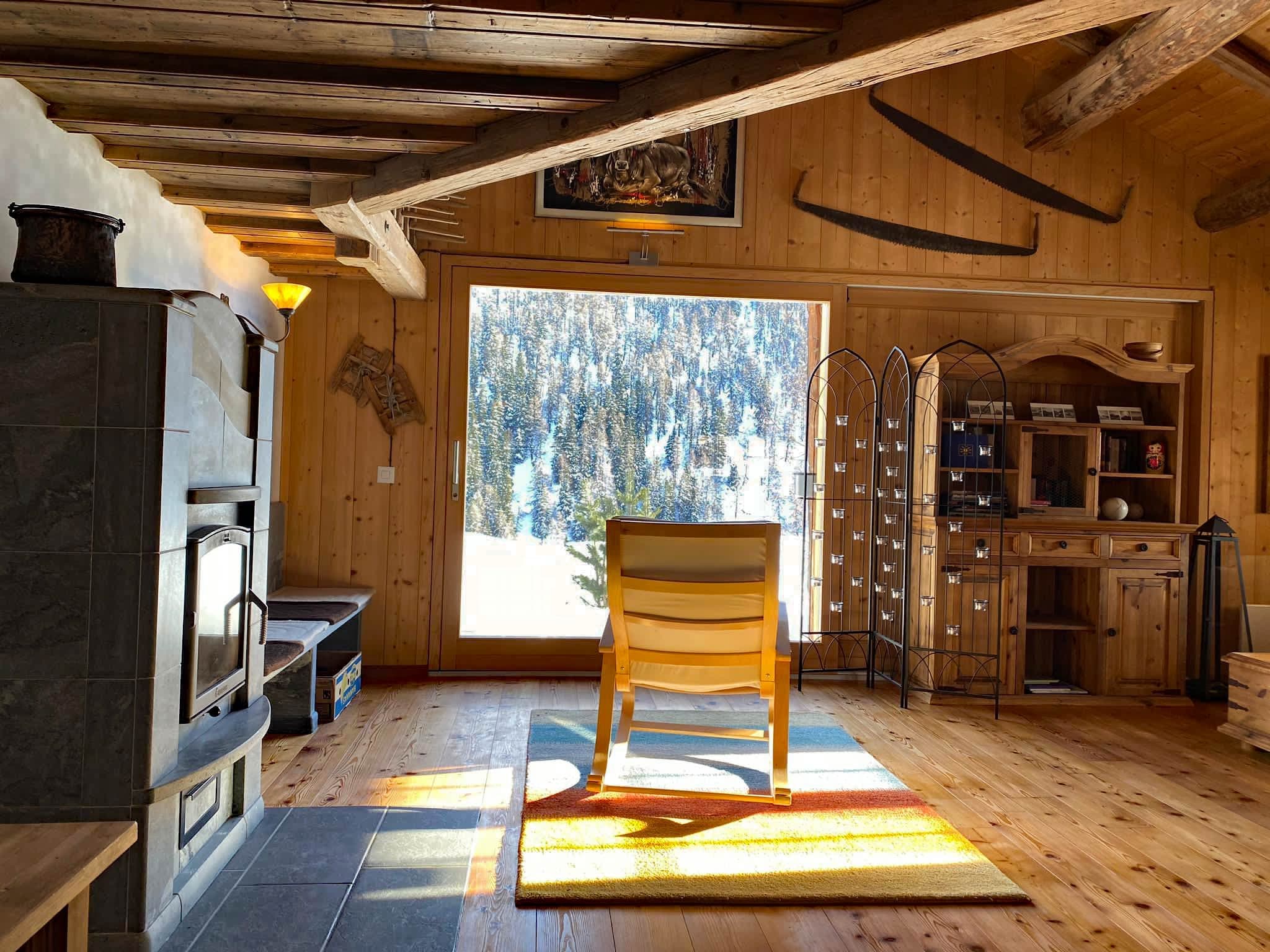 Schaukelstuhl am grossen Fenster der Wohnstube mit Blick auf die verschneite Bergwiese